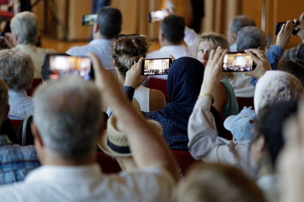 Spectators can be seen from behind, filming the stage program with their cell phones