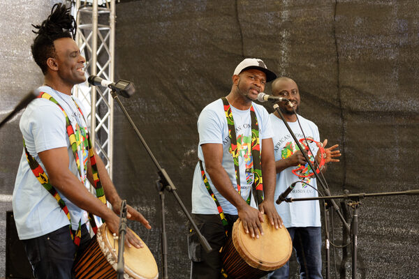 Three musicians stand on the stage and drum and clap their hands