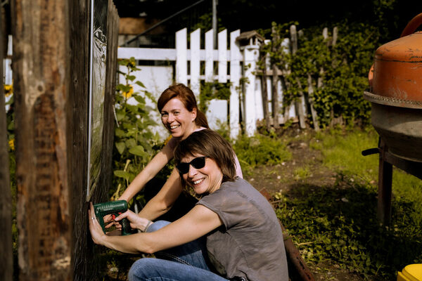 Aktionswoche 2022: Zwei Frauen befestigen mit einem Akkuschrauber eine Tafel an einer Holzwand