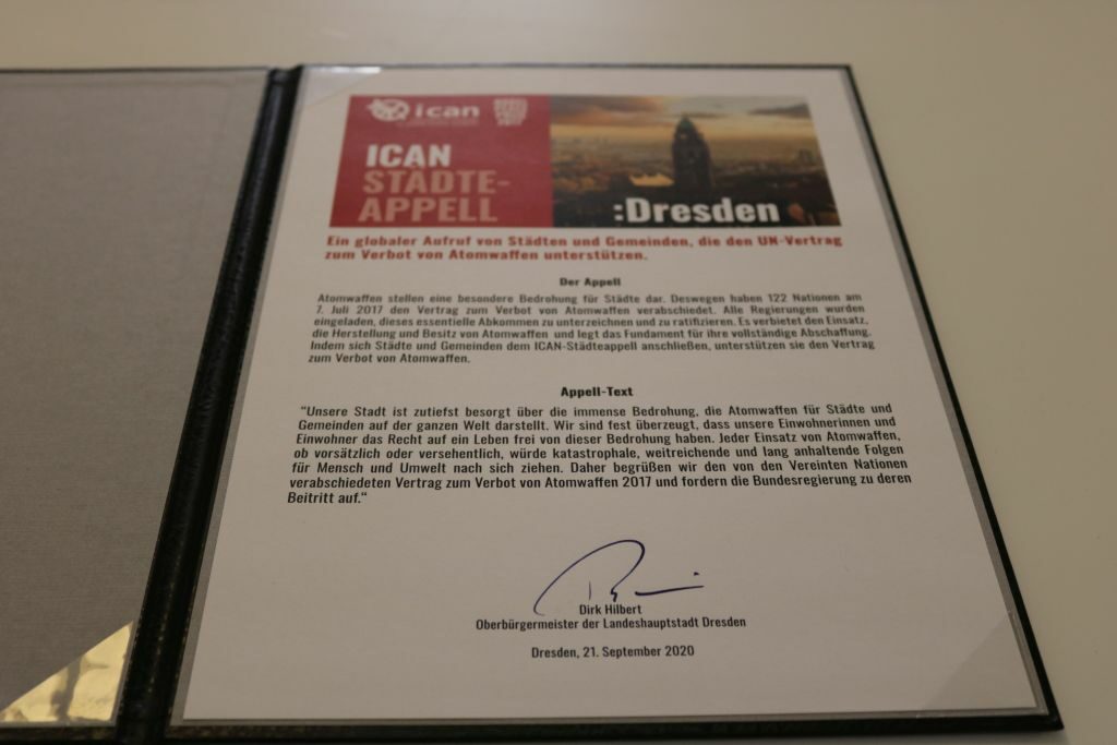 Dresdner Urkunde des ICAN-Städteappells zum Verbot von Atomwaffen mit Text, Logo von ICAN und einem Fotomotiv des Dresdner Rathausturm/Luftaufnahme