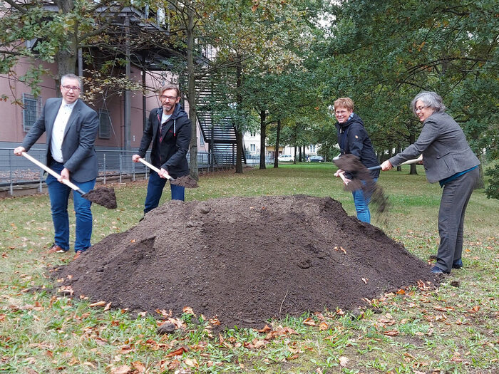 4 Menschen schaufeln mit einem Spaten Erde für den Baubeginn des Parkes