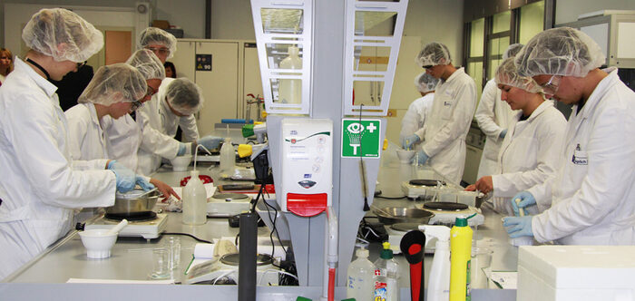 junge Leute in weißen Kitteln und mit Hauben arbeiten in einem Labor