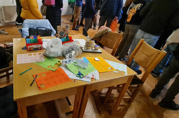 Tisch mit verschiedenen Materialien, im Hintergrund Kinder und Jugendliche