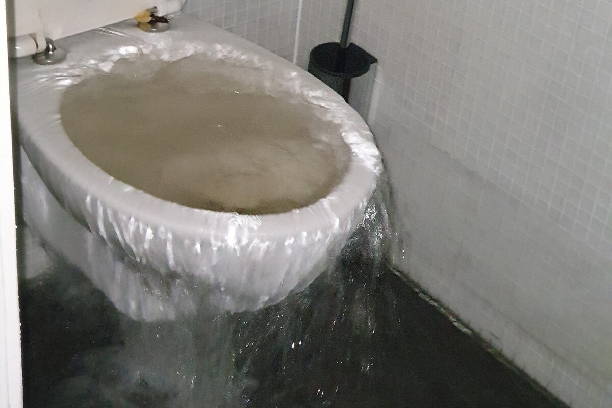Wasser sprudelt oben aus einer Toilette heraus.