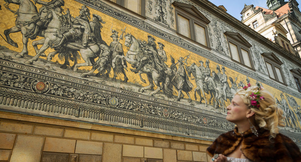 Foto vom Fürstenzug in Dresden, im Vordergrund eine barock gekleidete Dame