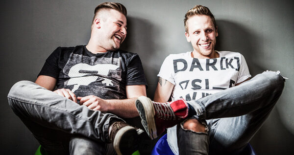 Zwei lachende Männer sitzen zurückgelehnt mit übergeschlagenen Beinen