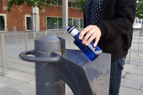 Eine blaue Trinkflasche wird am Trinkbrunnen befüllt.