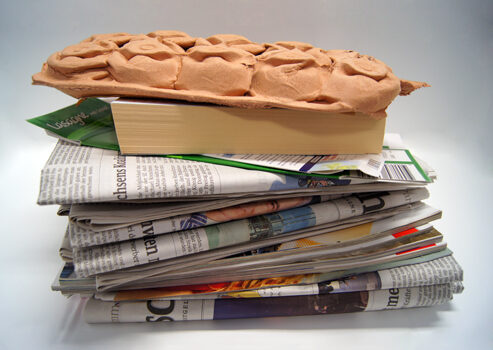 Das Bild zeigt einen Stapel Altpapier aus Zeitungen, einem Buch und einem Eierkarton
