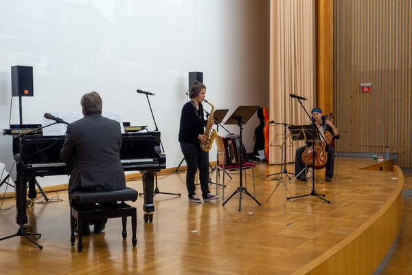 Drei Musiker*innen mit Klavier, Saxophon und Chello spielen auf der Bühne die interreligiöse Fanfare