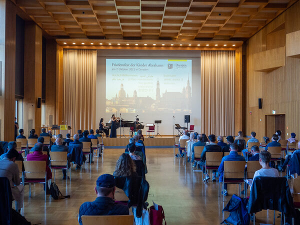 Das Publikum schaut auf die Bühne, wo das koreanische Ensemble musiziert. Auf der Leinwand dahinter ist ein Bild der Stadt Dresden eingeblendet.