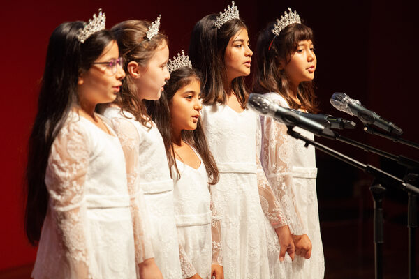 Fünf Mädchen aus dem Kinderchor des Forum Dialog stehen singend auf der Bühne. Sie tragen weiße Kleider und haben weiße Kronen auf dem Kopf.