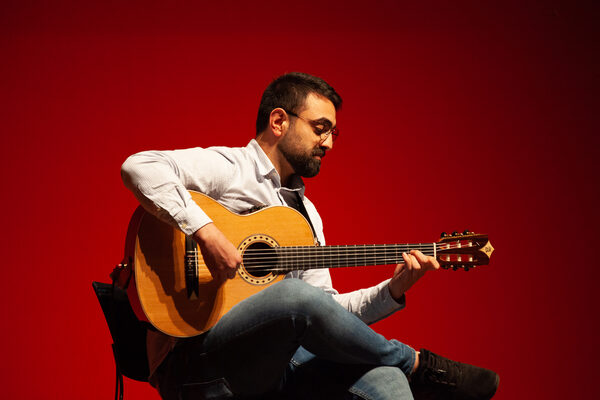 Künstler Mohamad Alsulaiman sitzt Gitarre spielend auf der Bühne.