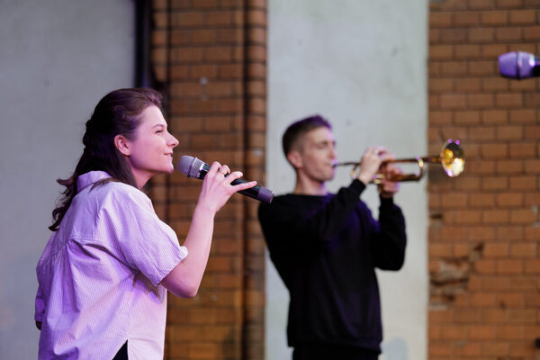 Die Sängerin Kateryna Kravchenko steht auf der Bühne und singt. Dahinter steht ein Mann, der Trompete spielt.