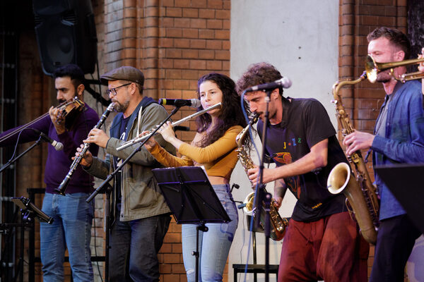 Fünf Musiker*innen der Banda Internationale mit verschiedenen Blas- und Streichinstrumenten stehen auf der Bühne.