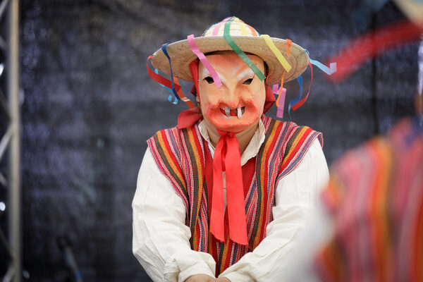 Eine Person mit Maske, Hut und bunter Kleidung tanzt auf der Bühne.