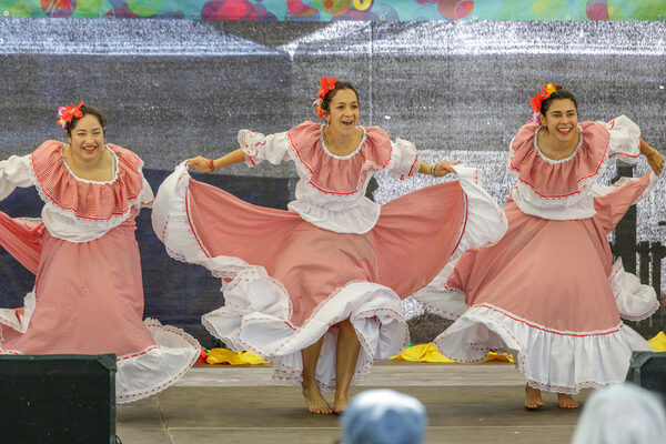 Drei Frauen mit rot-weißen Kleidern tanzen auf der Bühne.