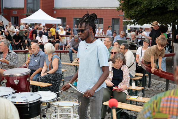Ein Trommler mit Sonnenbrille steht vor Publikum auf einem Platz