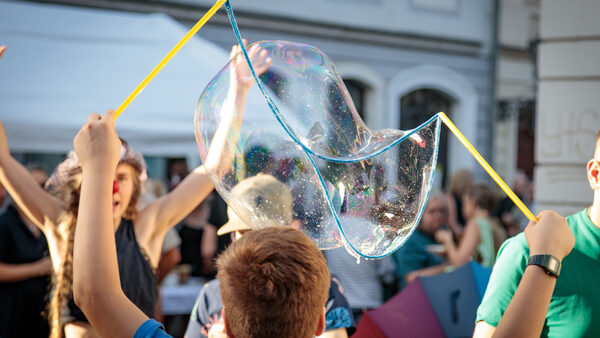 Eltern und Kinder spielen mit großen Seifenblasen beim Nachbarschaftsfest