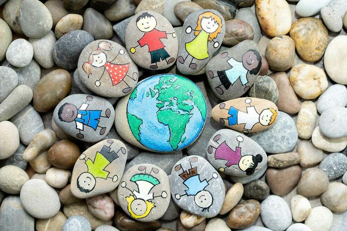 Strand mit Steinen, aus größeren flachen Steinen wird ein Bild gemacht: Erde und Kinder, die Hände halten