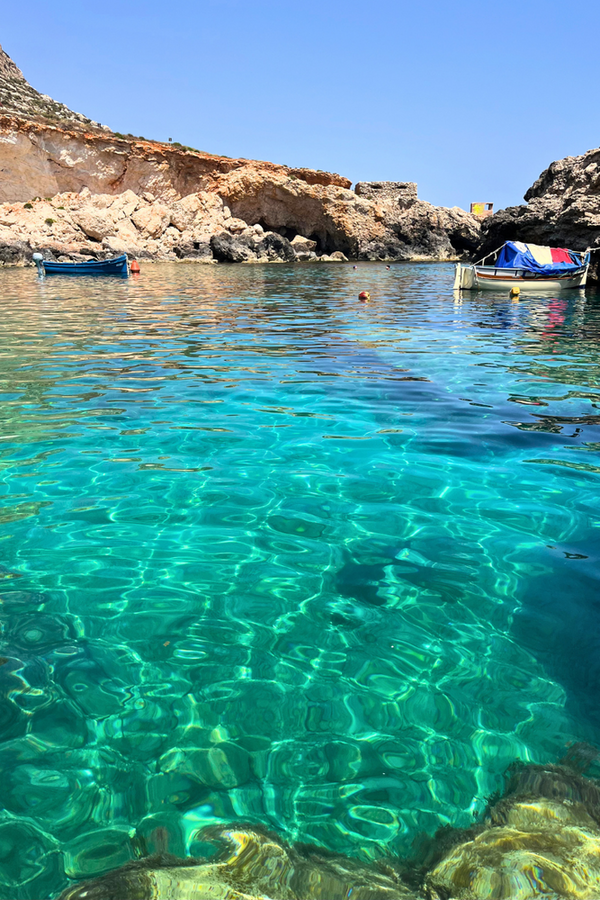 Malerische Bucht mit klarem, hellblauem Wasser, in dem mehrere kleine Boote liegen.