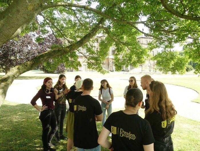 Jugendliche stehen in einem Kreis und sprechen miteinander, einige tragen ein schwarzes T-Shirt mit dem Logo der Landeshauptstadt Dresden