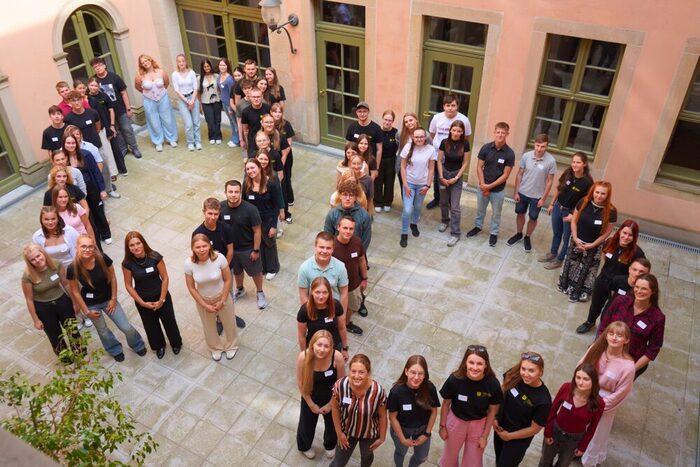 Gruppe junger Menschen in einem Innenhof bilden zweimal den Buchstaben D