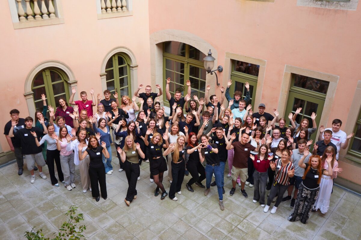Gruppe junger Menschen in einem Innenhof hebt freudig die Hände in die Luft