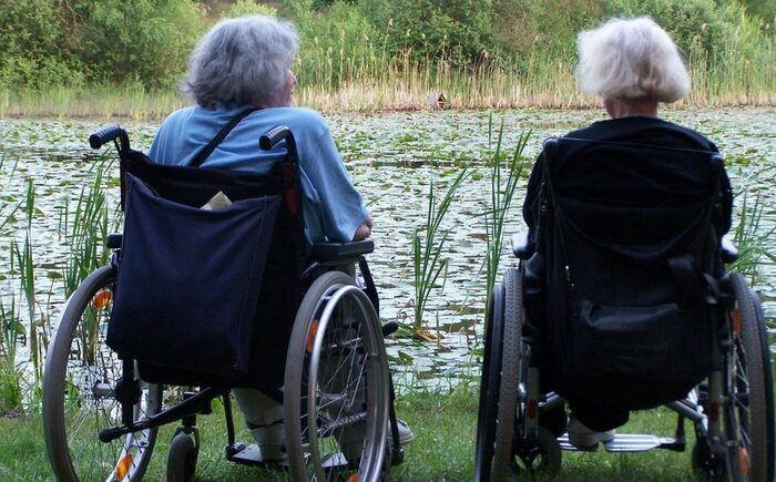 Zwei Seniorinnen sitzen im Rollstuhl am See.