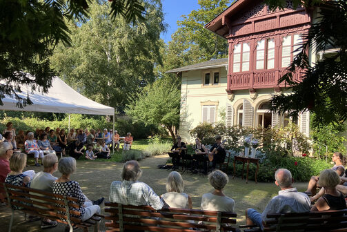 Besucher des Kraszewski-Museums lauschen dem Mandolinenkonzert mit Los Hermanos im Garten, im Schatten der Bäume.