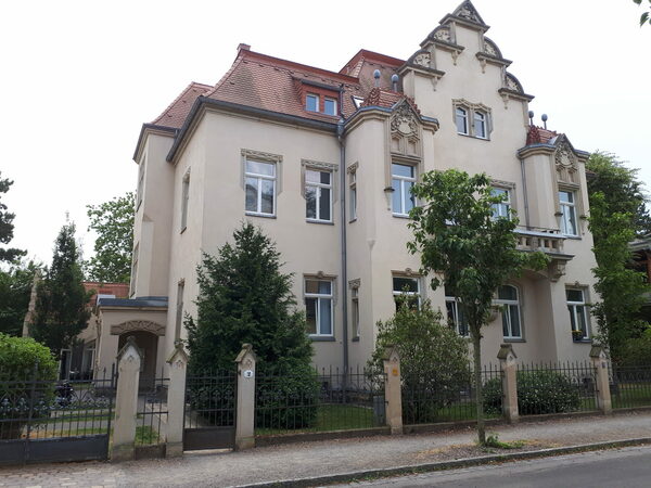 Arndtstraße 2: Die zweigeschossige Mietvilla mit leicht rosefarbener Putzfassade und Sandsteinverzierungen erinnert mit ihrem Stufengiebel an die Formensprache der Gotik. Das Dach ist rot eingedeckt. Im Obergeschoss findet sich ein repräsentativer Balkon. Das Grundstück ist mit einem Eisenzaun umfriedet.