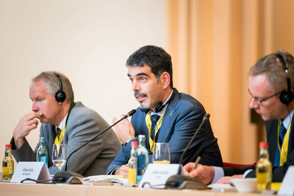 Bürgermeister Eneko Goia von Donostia-San Sebastián spricht über die Erfahrungen in seiner Stadt, zwei Teilnehmer sitzen an seiner Seite