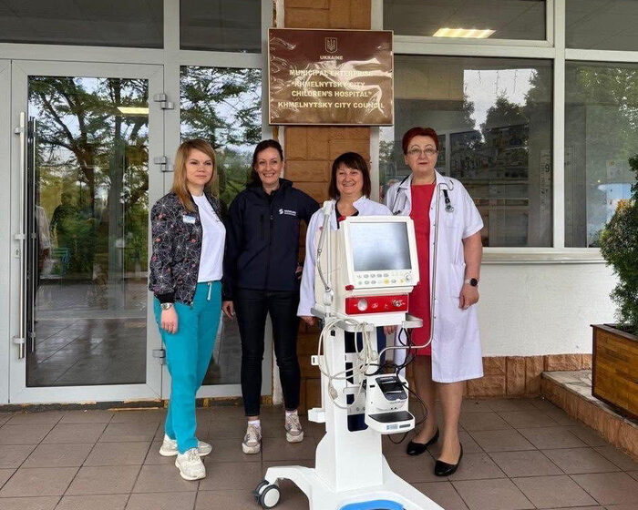 Vier Frauen stehen mit einem Beatmungsgerät vor einem Kinderkrankenhaus