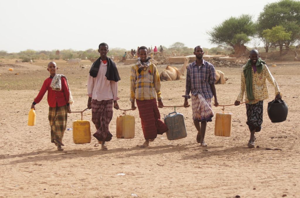 Männer mit Wasserkanistern auf dem Weg zur Wasserstelle in der von Dürre gezeichneten Landschaft