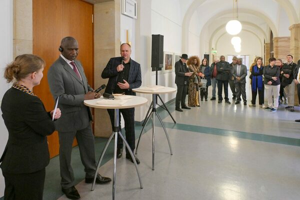Drei Personen diskutieren an Stehtischen, im Hintergrund hören Menschen zu
