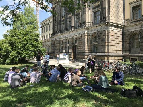 Junge Menschen sitzen auf der Wiese vor der Hochschule für Musik und unterhalten sich
