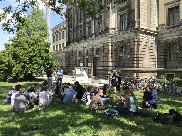 Junge Menschen sitzen auf der Wiese vor der Hochschule für Musik und unterhalten sich