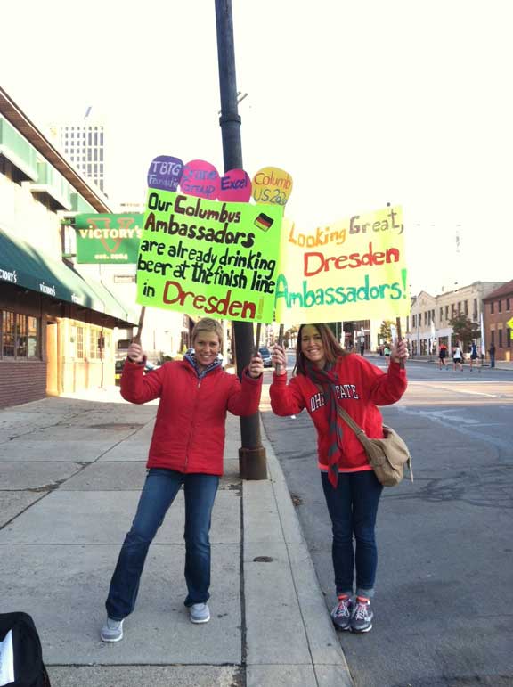 2 Frauen halten Schilder mit Anfeuerungssprüchen in der Hand, während sie an der Marathonstrecke stehen