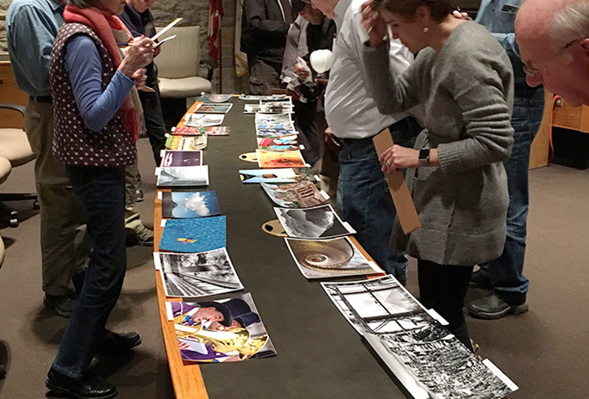 Eine Gruppe von Menschen schaut Fotos an, die auf einem Tisch liegen.