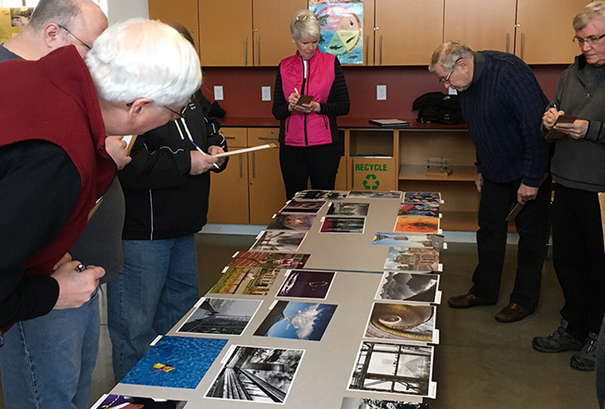 Eine Gruppe von Menschen schaut Fotos an, die auf einem Tisch liegen.