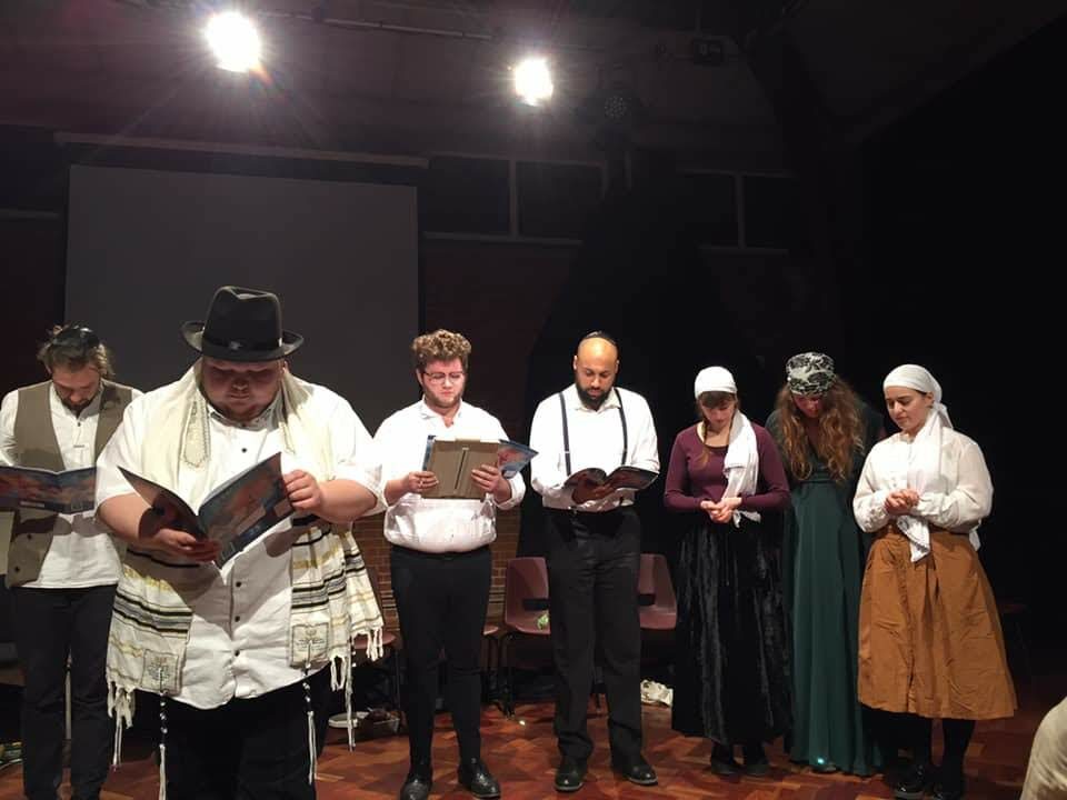 Szene aus dem Theaterstück "Train of Life" mit einer größeren Gruppe von Schauspielern, die Dorfbewohner darstellen