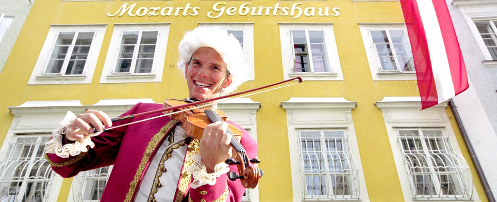 Mozart-Stadt Salzburg: Zu sehen ist ein Mozart-Darsteller mit Violine vor Fassade des Mozart-Geburtshauses