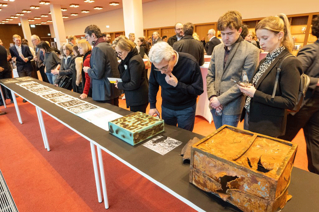 Menschen bei den Exponaten der "Dresden-Kassette", bestehend aus einer beschädigten Eisenkiste, einem Bombensplitter und weiteren Ausstellungsstücken