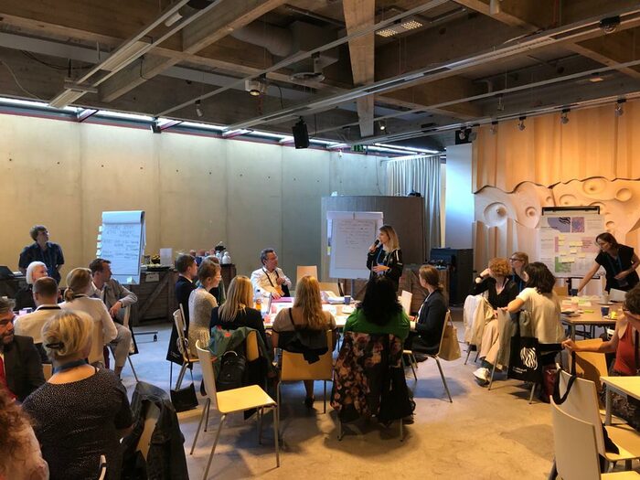 Sitzgruppen in einem Raum, eine Person mit Mikrofon steht