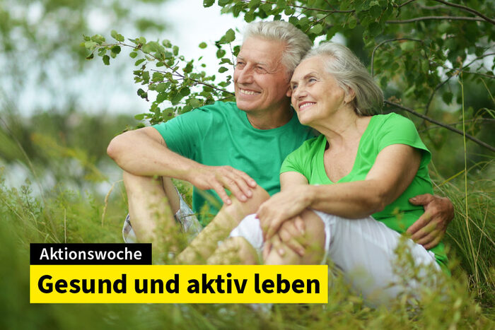 Eine ältere Frau und ein älterer Mann sitzen zusammen in fröhlicher Stimmung in der Natur.
