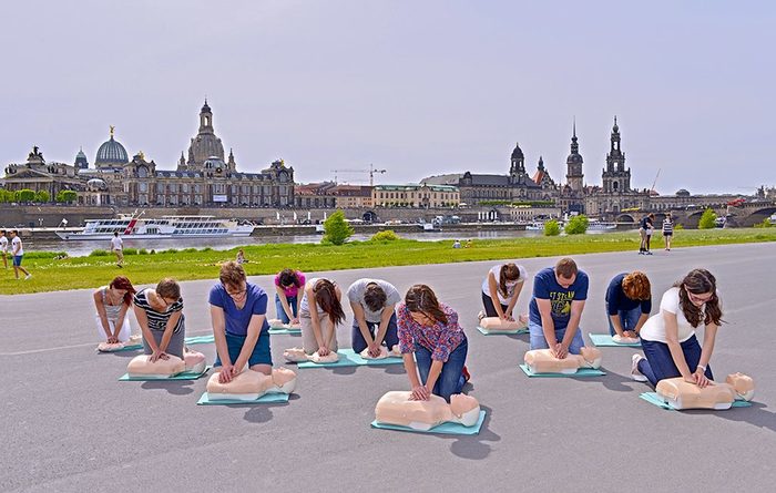 Eine Gruppe junger Menschen übt die Reanimation an Puppen von der Stadtsilhouette von Dresden
