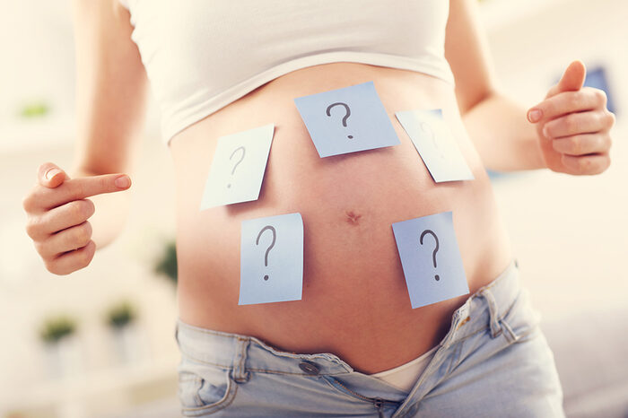 Foto von einer schwangeren Frau mit Fragezeichen auf dem Bauch