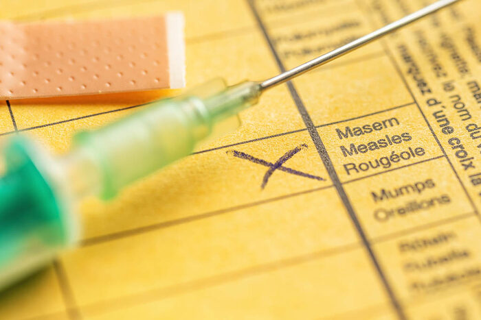 Makroaufnahme eines Impfausweises, die Masernschutzimpfung ist angekreuzt. Auf dem Ausweis liegen ein Pflaster und eine Spritze.
