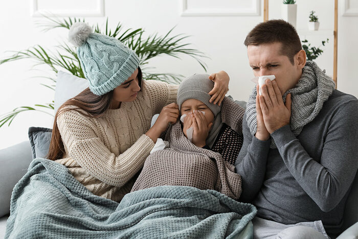 eine an Grippe erkrankte junge Familie sitzt zusammen auf dem Sofa zu Hause