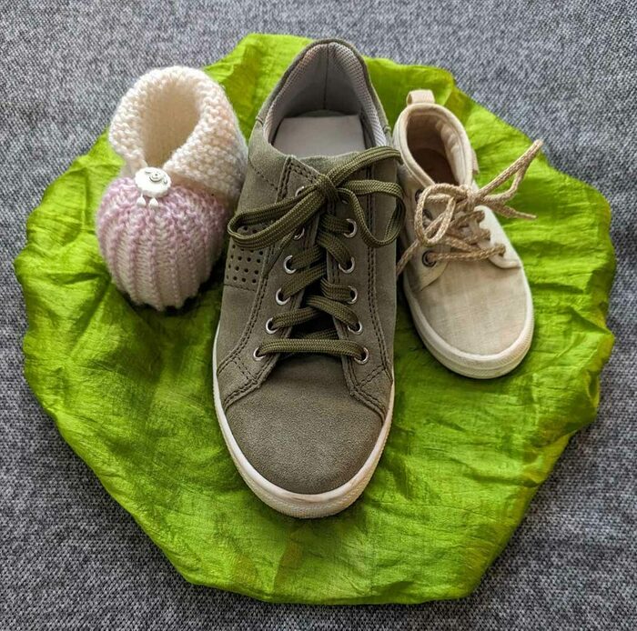 Schuh eines Erwachsenen und auf beiden Seiten jeweils ein Kinder- bzw. Babyschuh