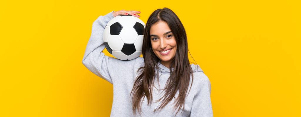 junge Frau mit Fußball auf der Schulter; der Hintergrund ist gelb